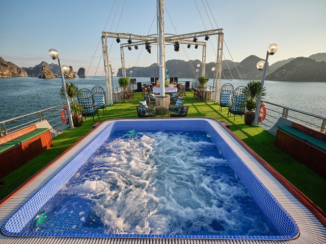 Scenic view of a luxury cruise deck with hot tub, overlooking Halong Bay's limestone islands and cal.