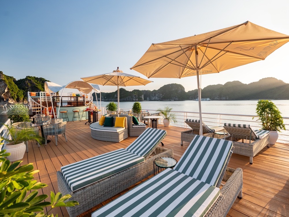 Relaxing lounge area on Serenity Cruise in Lan Ha Bay with sunbeds, umbrellas, and scenic water view.