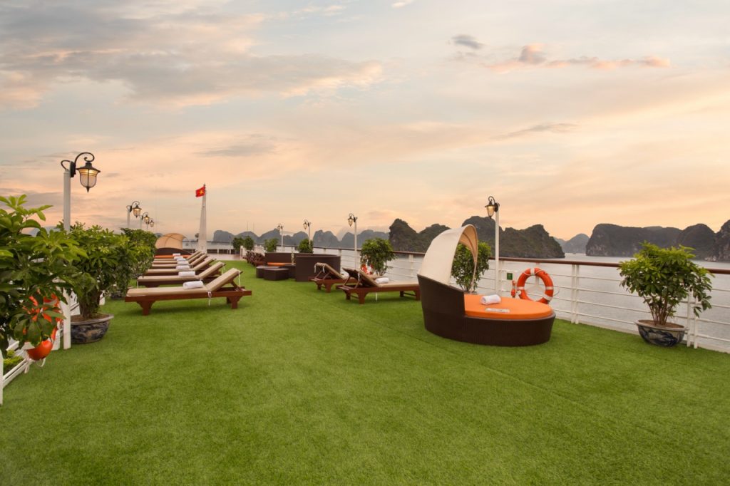 Sunset view from the outdoor deck of Mon Cheri Cruise in Halong Bay, featuring lounge chairs and lus.