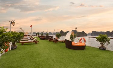 Sunset view from the outdoor deck of Mon Cheri Cruise in Halong Bay, featuring lounge chairs and lus.