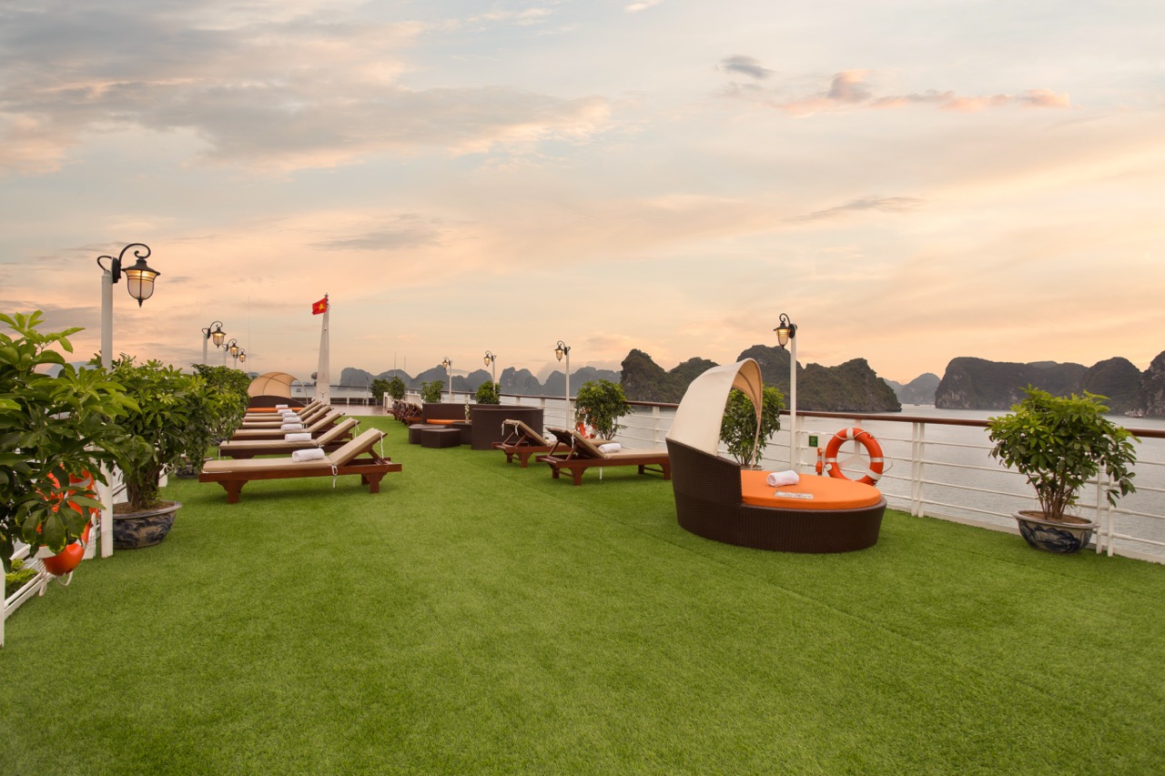 Sunset view from the outdoor deck of Mon Cheri Cruise in Halong Bay, featuring lounge chairs and lus.