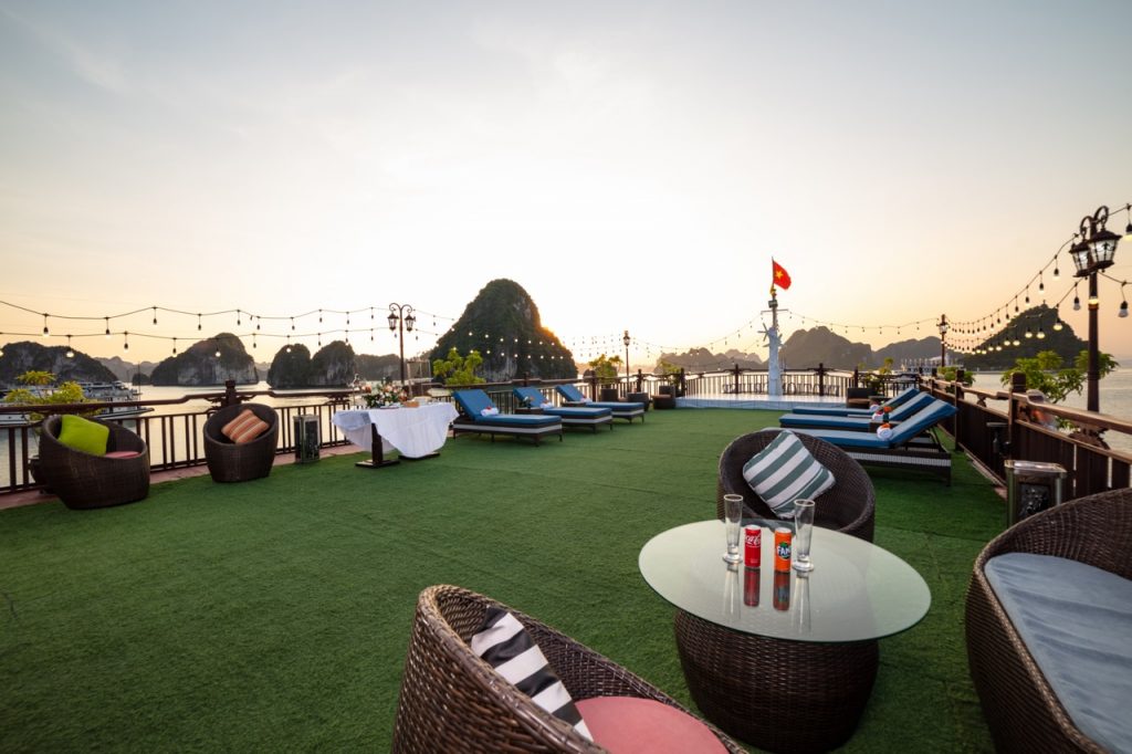 Stunning terrace view with lounging chairs and string lights over Halong Bay at sunset.