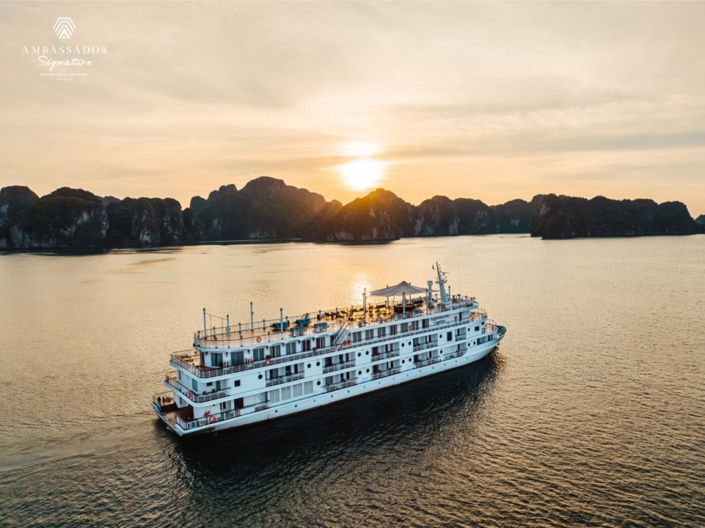 A scenic view of a luxury cruise sailing through Halong Bay at sunset, showcasing stunning limestone.
