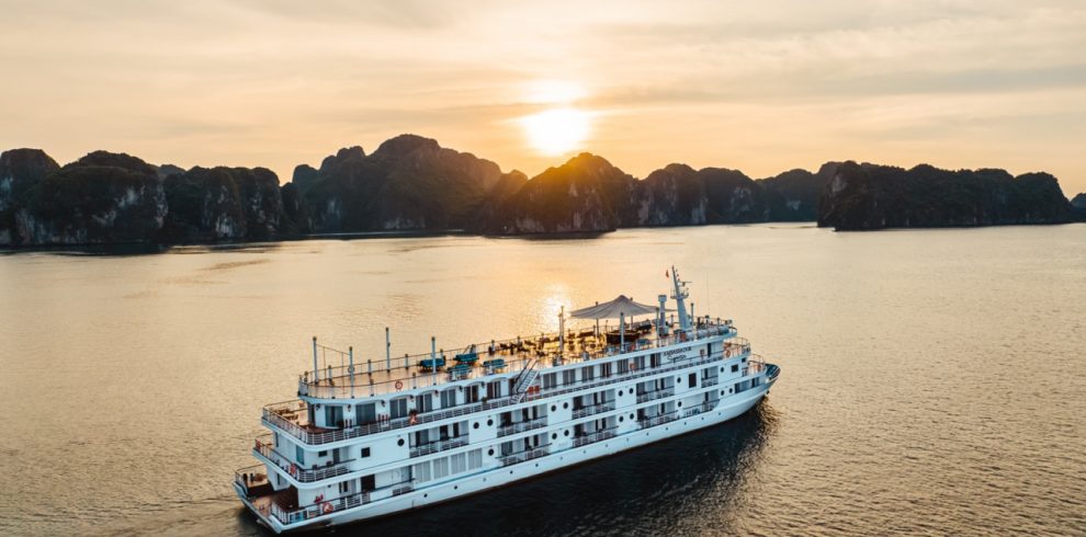 A scenic view of a luxury cruise sailing through Halong Bay at sunset, showcasing stunning limestone.