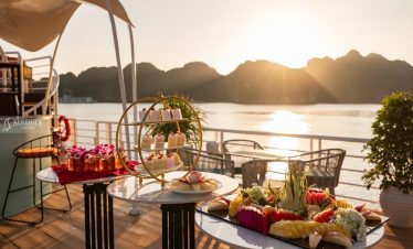 Beautiful scene of a luxurious cruise deck with a sunset view over Lan Ha Bay, featuring a table set.