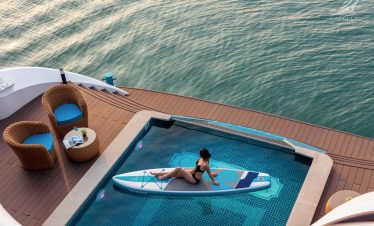 Woman relaxing on paddleboard in infinity pool overlooking the sea, luxury yacht cruise experience. - Capella Cruise Halong Bay
