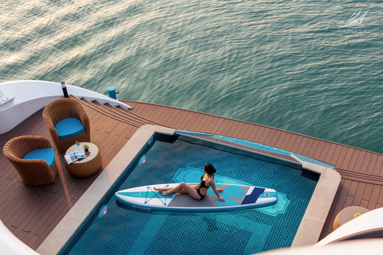 Woman relaxing on paddleboard in infinity pool overlooking the sea, luxury yacht cruise experience. - Capella Cruise Halong Bay