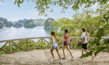 Beautiful group of travelers walking along a scenic trail overlooking Halong Bay, lush greenery and.