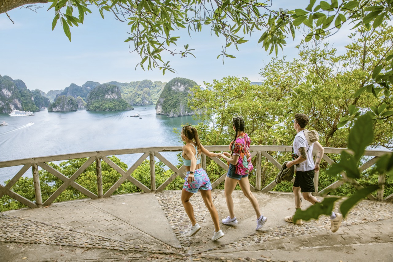 Beautiful group of travelers walking along a scenic trail overlooking Halong Bay, lush greenery and.