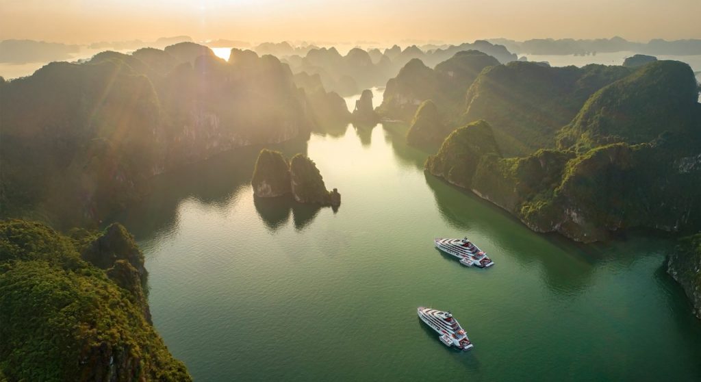 Vietnameses natural landscape with limestone karsts and cruising boats at sunset.