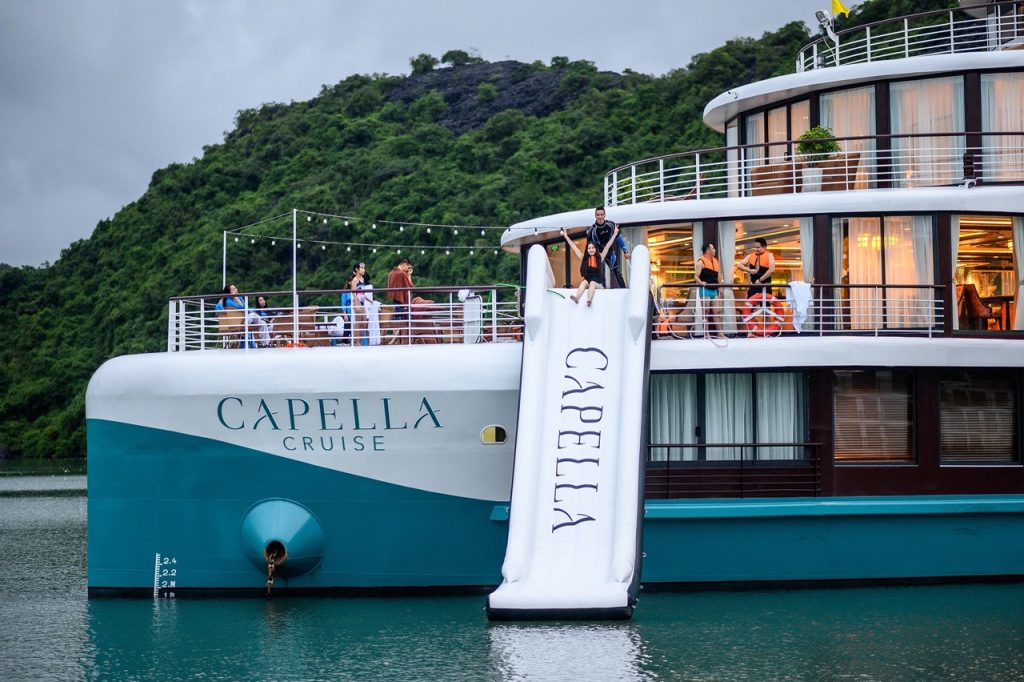 Luxurious Capella Cruise ship on the water with scenic green hills in the background.