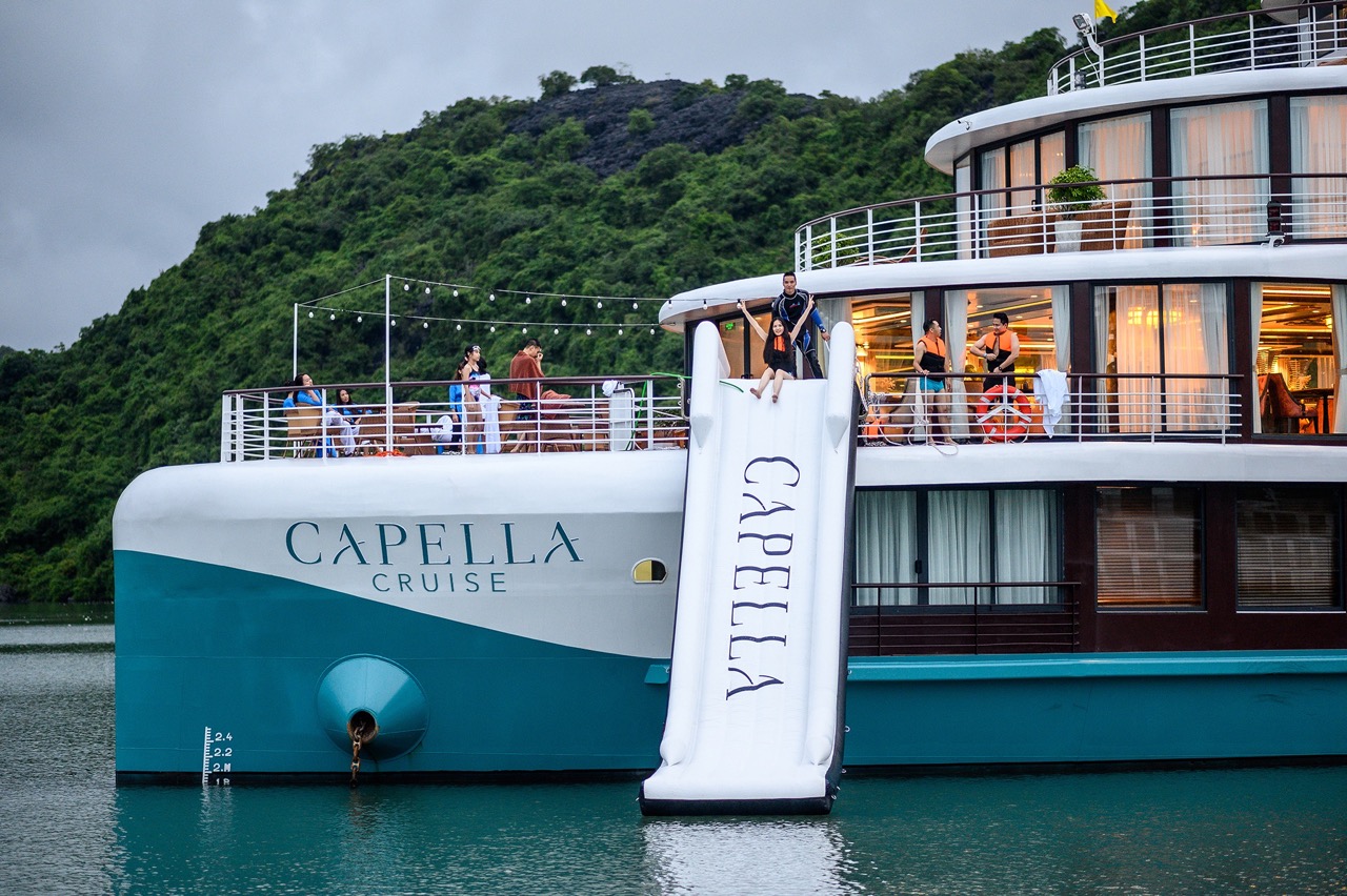 Luxurious Capella Cruise ship on the water with scenic green hills in the background.