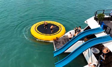 Vivid scene of tourists enjoying a fun water slide and swimming on Lan Ha Bay cruise, surrounded by.