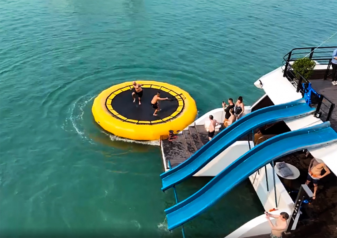 Vivid scene of tourists enjoying a fun water slide and swimming on Lan Ha Bay cruise, surrounded by.