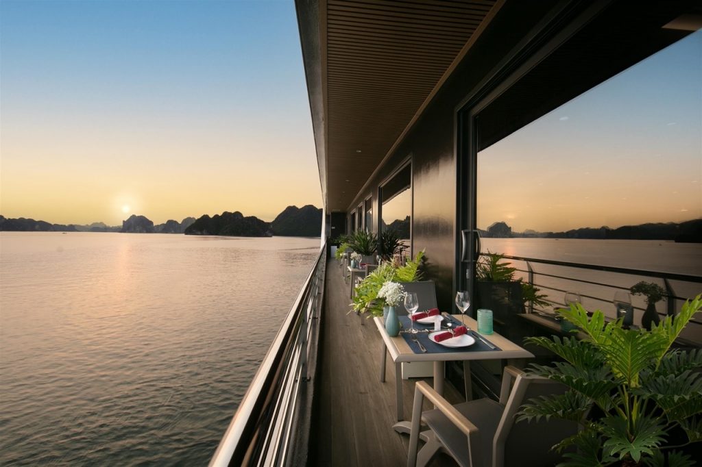 Sunset view from cruise balcony in Halong Bay with calm waters and scenic limestone karsts.
