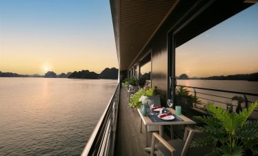Sunset view from cruise balcony in Halong Bay with calm waters and scenic limestone karsts.