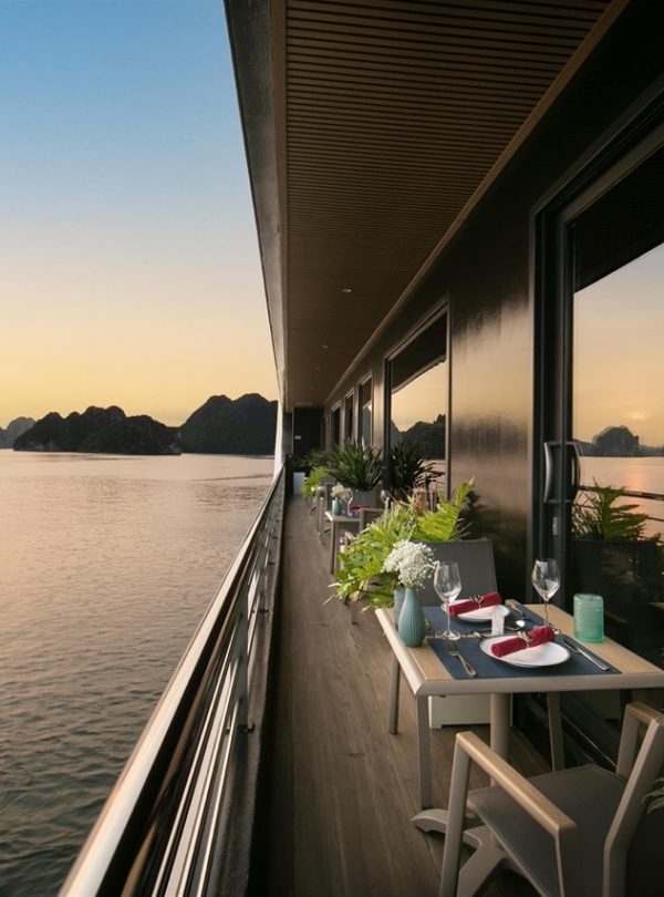Sunset view from cruise balcony in Halong Bay with calm waters and scenic limestone karsts.
