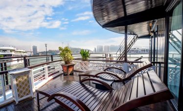 Balcony view of Halong Bay with lounge chairs and lush city skyline in the background.