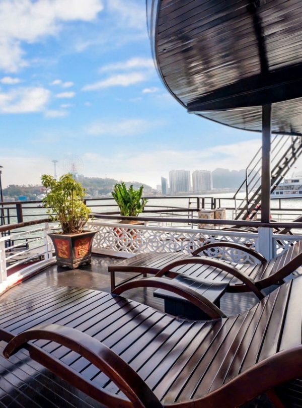 Balcony view of Halong Bay with lounge chairs and lush city skyline in the background.