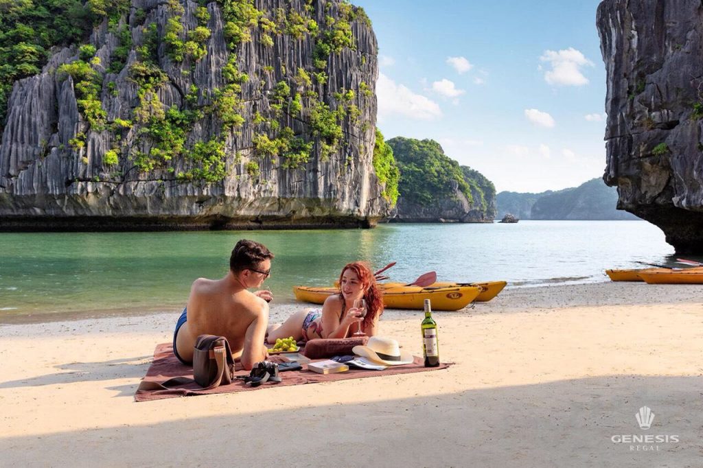 Scenic view of a couple relaxing on the beach with limestone karsts and emerald waters in Halong Bay.