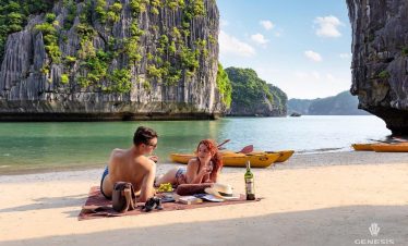 Scenic view of a couple relaxing on the beach with limestone karsts and emerald waters in Halong Bay.