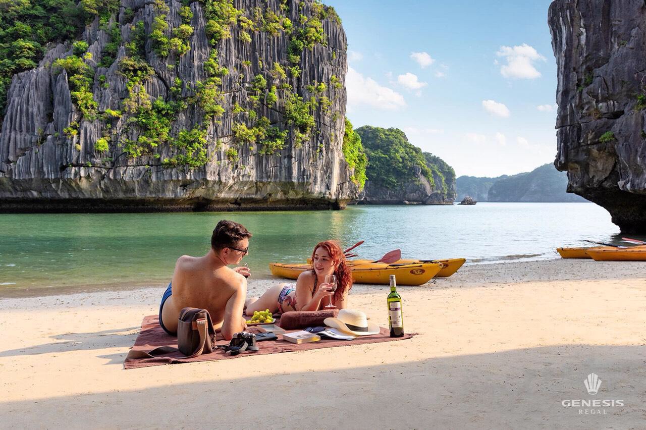 Scenic view of a couple relaxing on the beach with limestone karsts and emerald waters in Halong Bay.