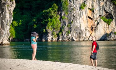 Stunning view of two travelers on the beach with limestone cliffs and lush greenery in Halong Bay, V.