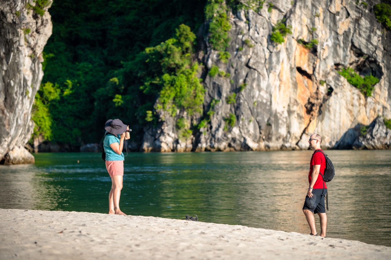 Stunning view of two travelers on the beach with limestone cliffs and lush greenery in Halong Bay, V.