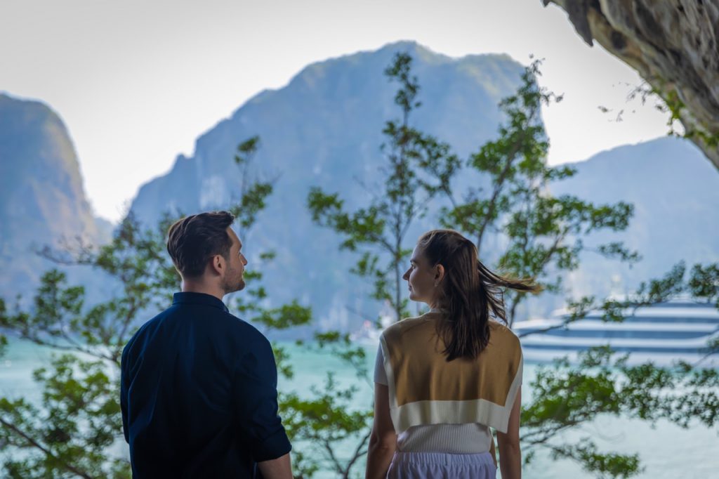 Romantic couple enjoying Halong Bay cruise balcony with lush green islands in the background.