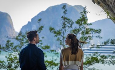 Romantic couple enjoying Halong Bay cruise balcony with lush green islands in the background.