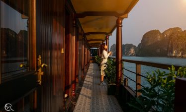 Scenic view of Halong Bay from a cruise balcony with lush islands and calm waters at sunset.