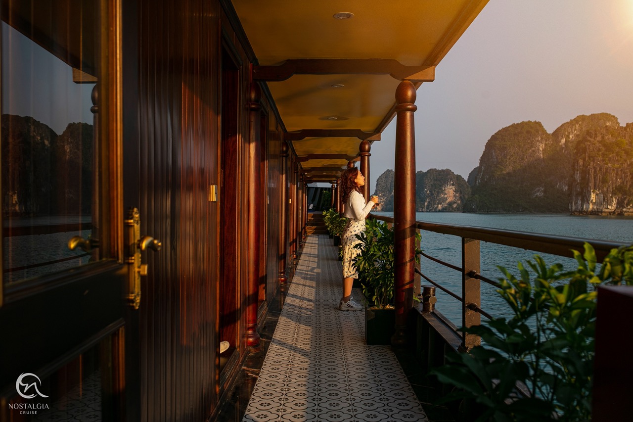 Scenic view of Halong Bay from a cruise balcony with lush islands and calm waters at sunset.