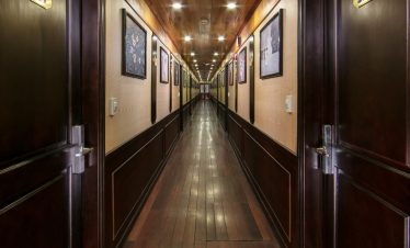 A long corridor inside a luxury Halong Bay cruise ship with wooden walls and doors.