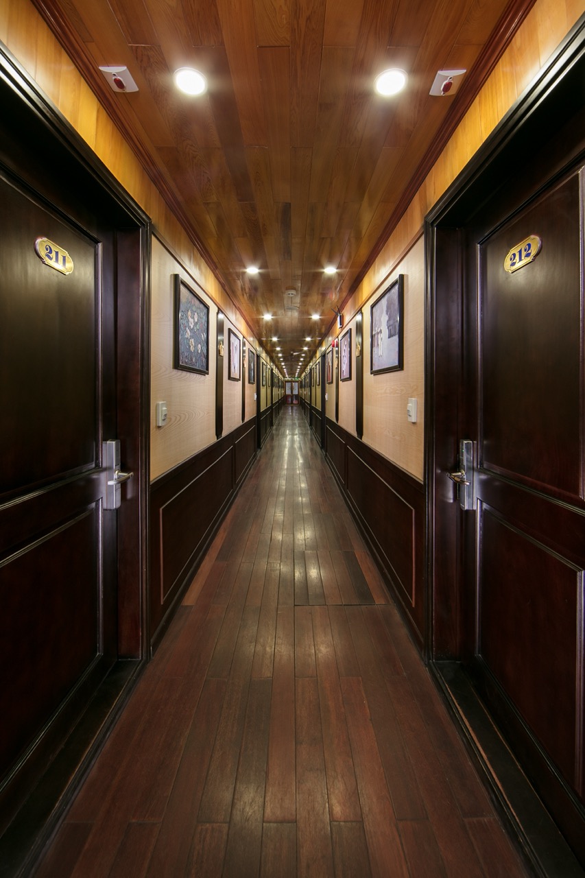 A long corridor inside a luxury Halong Bay cruise ship with wooden walls and doors.