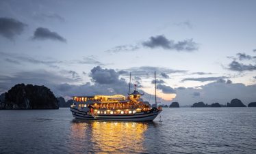 A luxurious cruise ship sailing through the scenic waters of Bai Tu Long Bay at sunset.