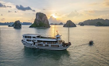 Sunset view of Renea Cruise sailing through Halong Bay's limestone karsts at dusk, creating a tranqu.