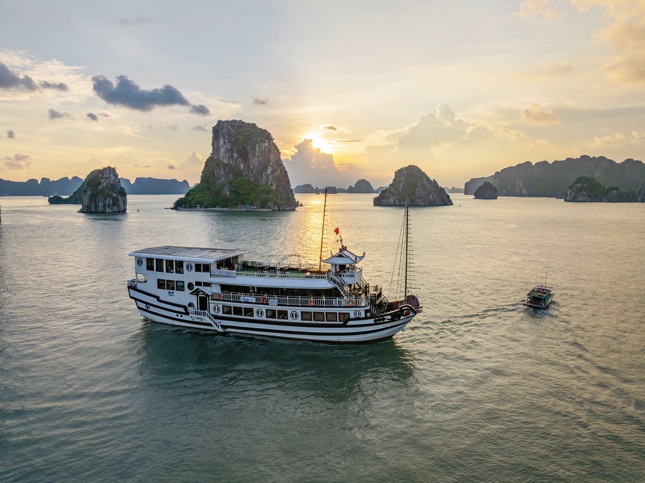 Sunset view of Renea Cruise sailing through Halong Bay's limestone karsts at dusk, creating a tranqu.