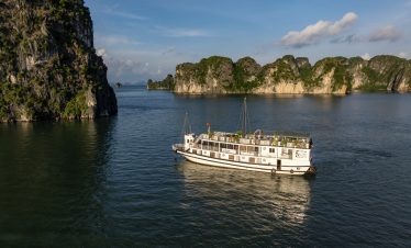 Scenic view of a cruise boat sailing through Halong Bay's limestone karsts and emerald waters.