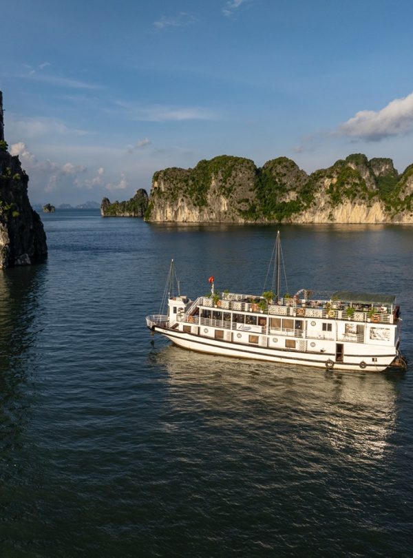 Scenic view of a cruise boat sailing through Halong Bay's limestone karsts and emerald waters.