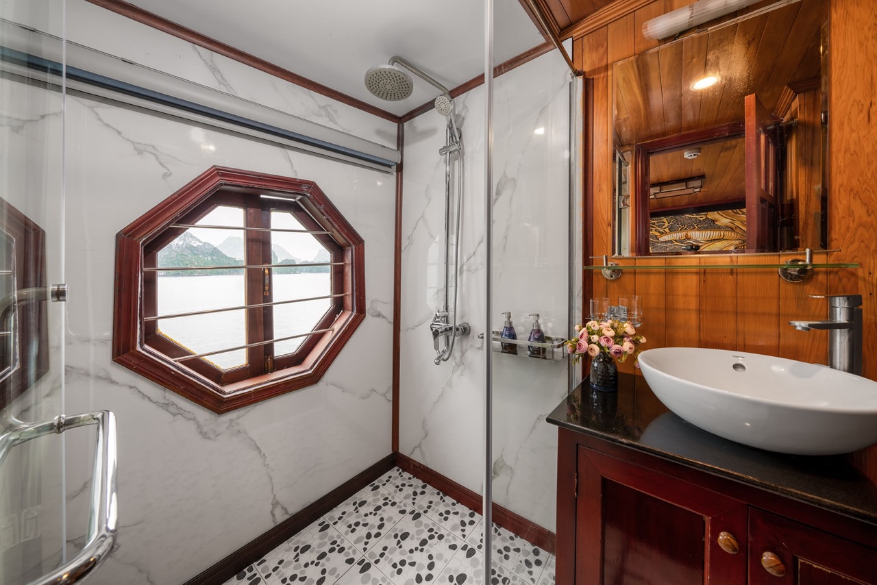 A luxurious cruise bathroom with elegant marble finishes and a unique octagonal window overlooking H.