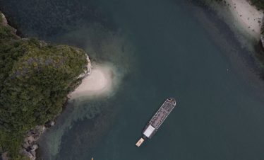 Aerial view of a cruise boat sailing in Halong Bay surrounded by emerald waters and towering limesto.