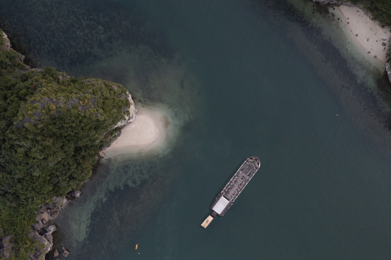 Aerial view of a cruise boat sailing in Halong Bay surrounded by emerald waters and towering limesto.