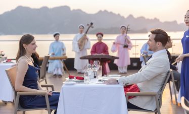 Romantic scene of a couple dining on Calista Cruise in Halong Bay during sunset, with traditional mu.