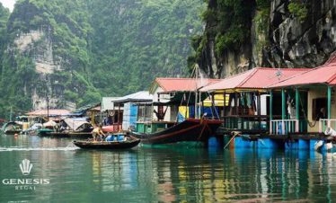 Scenic view of floating houses and boats on Halong Bay with lush green cliffs in the background.