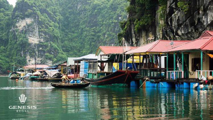 Scenic view of floating houses and boats on Halong Bay with lush green cliffs in the background.