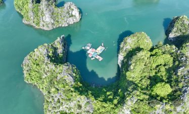 Aerial view of Halong Bay with towering limestone islands and a cruise boat, showcasing scenic beaut.