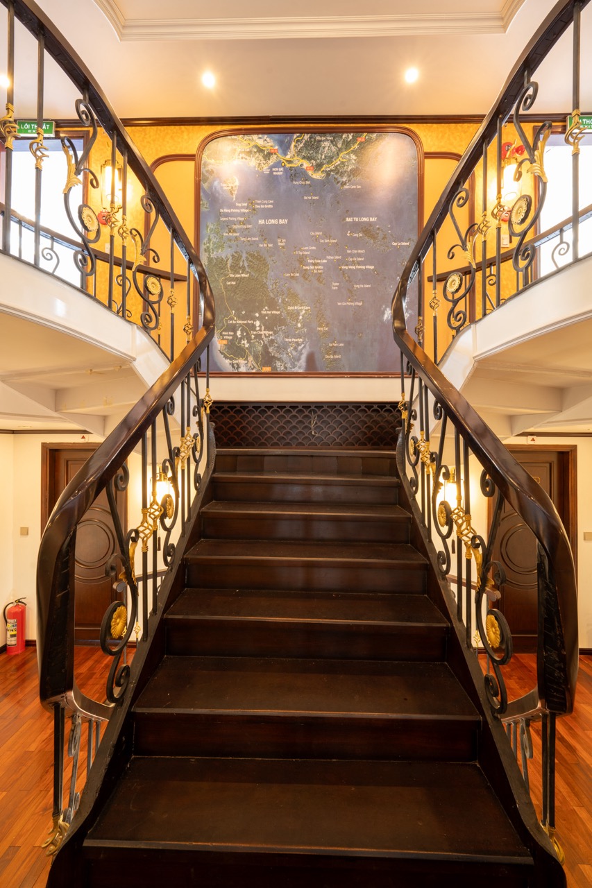 Elegant staircase inside Bai Tu Long cruise ship with classic design and warm lighting.