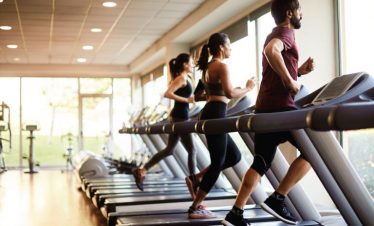 Running on treadmill in gym with large windows and natural light.