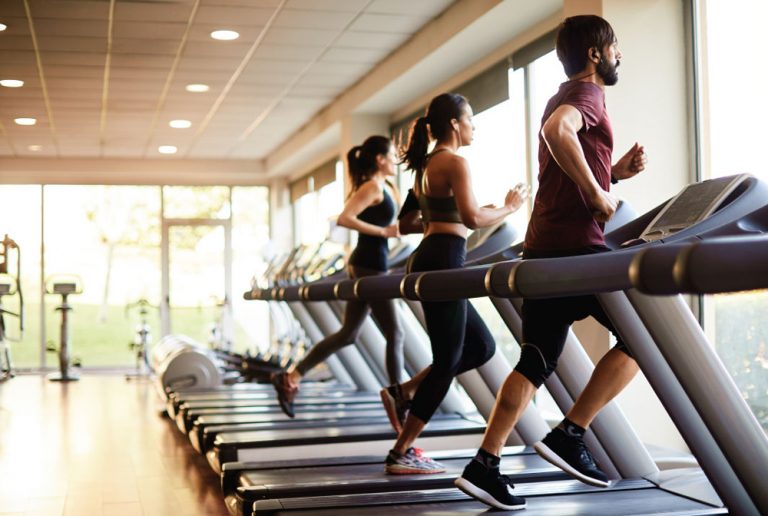 Running on treadmill in gym with large windows and natural light.