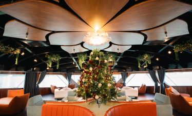 Cozy boat interior with Christmas decorations, plush seating, and scenic water views.